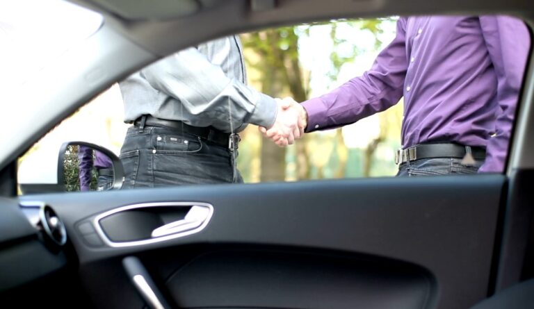 Two men shake hands outside a car