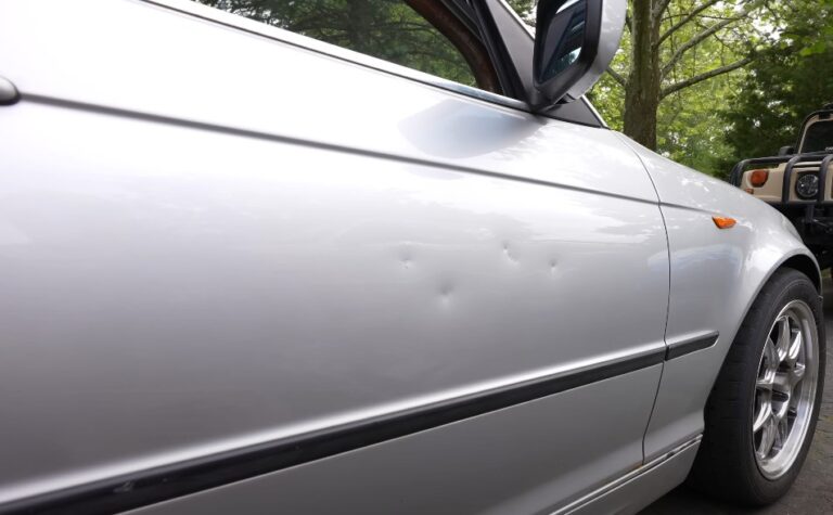 A silver car door, marred by several small dents