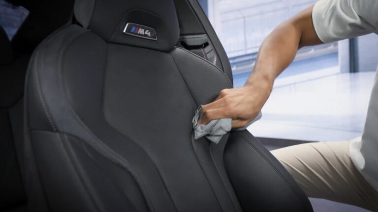 A Person Wiping Down BMW’s Car Seats with A Cloth, Focusing on Cleaning the Black Leather Surface