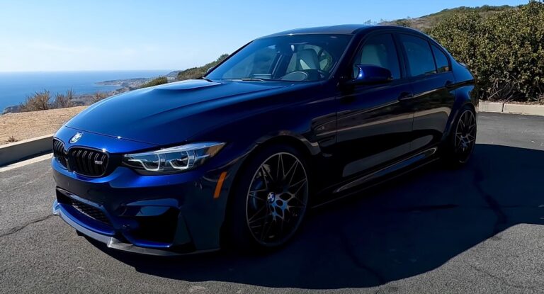 Deep blue BMW M3, showcasing a sleek profile against a backdrop of coastal scenery