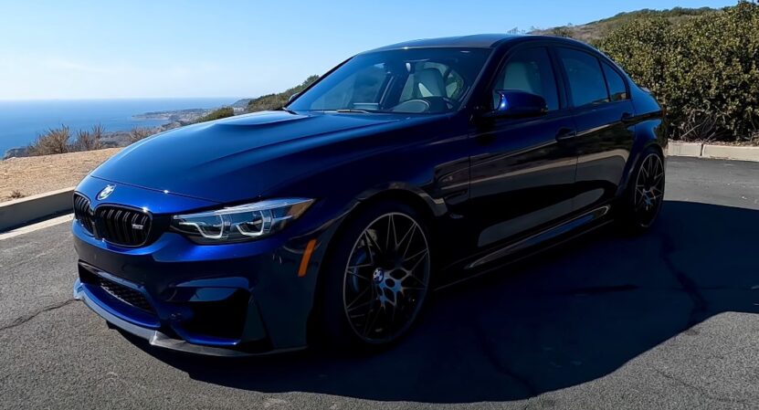 Deep blue BMW M3, showcasing a sleek profile against a backdrop of coastal scenery