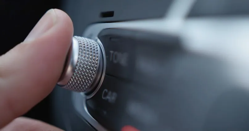 A finger delicately adjusts the car's audio