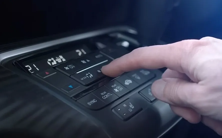 A finger presses a button, adjusting the car's climate control