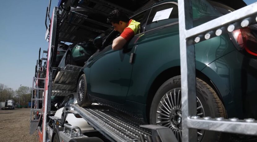A dark green car is loaded onto a specialized transport vehicle