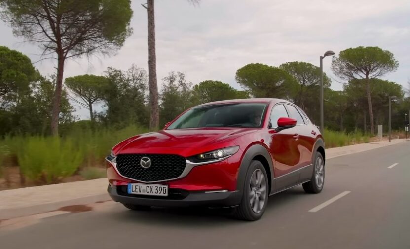 A red Mazda CX-30 SUV cruises along a paved road