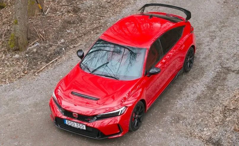 A vibrant red Honda Civic Type R parked on a gravel path