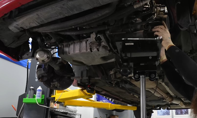 A mechanic works on the underside of a lifted vehicle