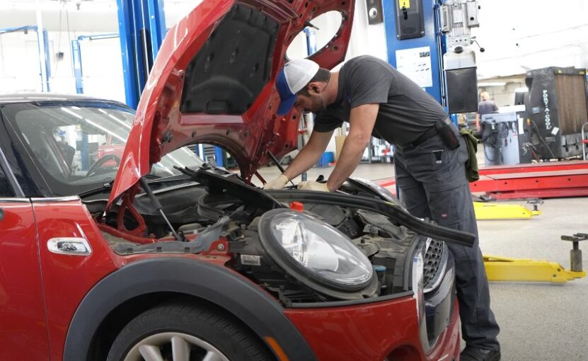 A mechanic inspects a red Mini Cooper's engine compartment