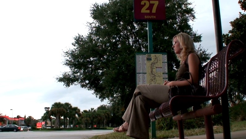 A woman sits patiently at a bus stop