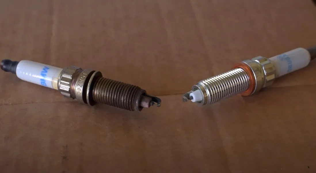 Two spark plugs resting on a cardboard box, showcasing their metallic finish and threaded ends