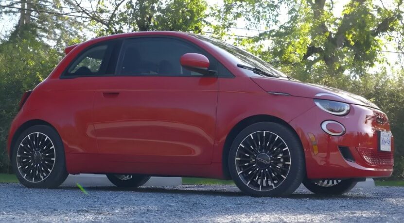 A vibrant red Fiat 500 car, parked on a gravel surface