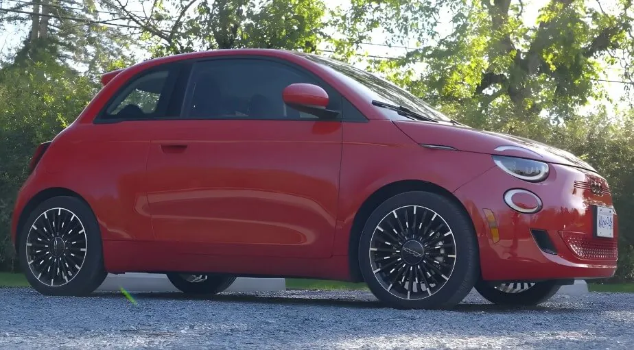 A vibrant red Fiat 500 car, parked on a gravel surface