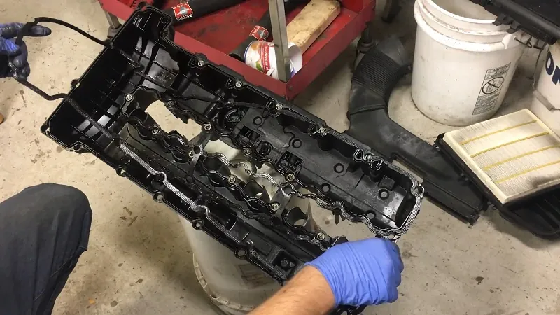 Mechanic holding a valve cover with an attached gasket removed from a BMW engine