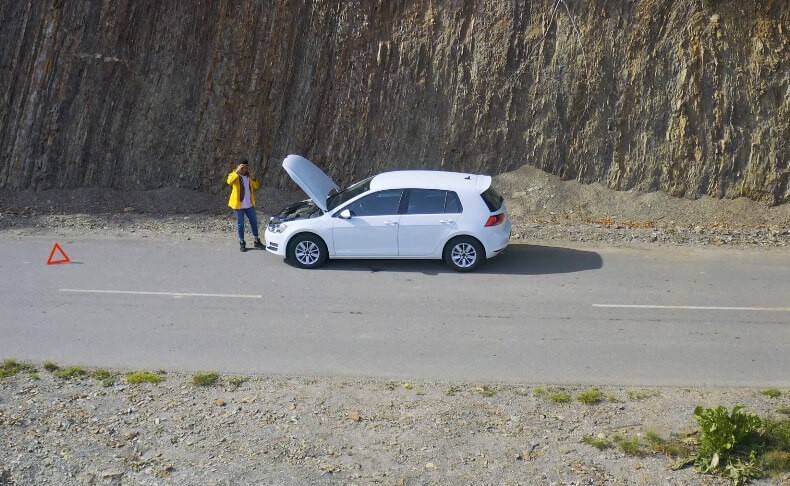 A person stands beside her broken-down car, a warning triangle placed for safety