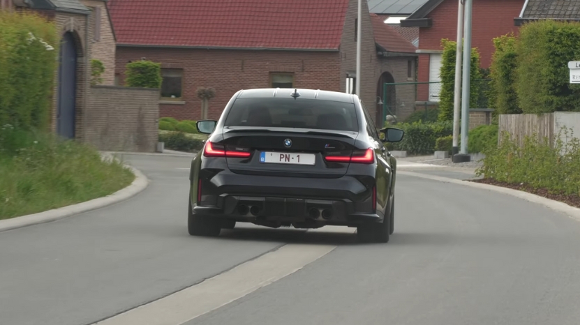 A black BMW M3 drives through a quiet neighborhood street