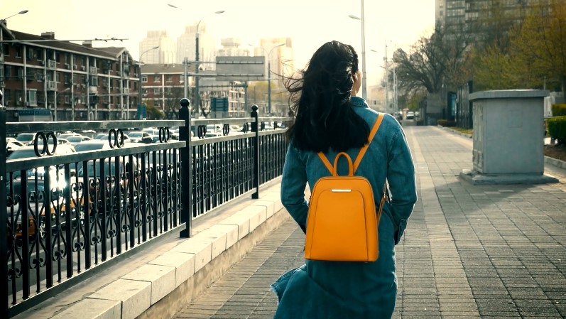A woman with a orange backpack strolls down a city street