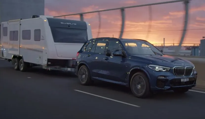 A sleek blue BMW X5 towing a stylish white camper trailer on a highway