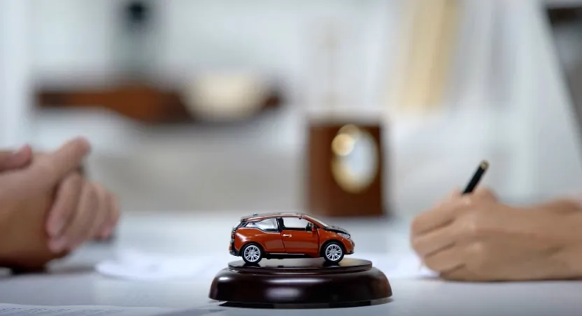 A miniature car sits on a wooden stand, amidst paperwork, symbolizing a settlement agreement