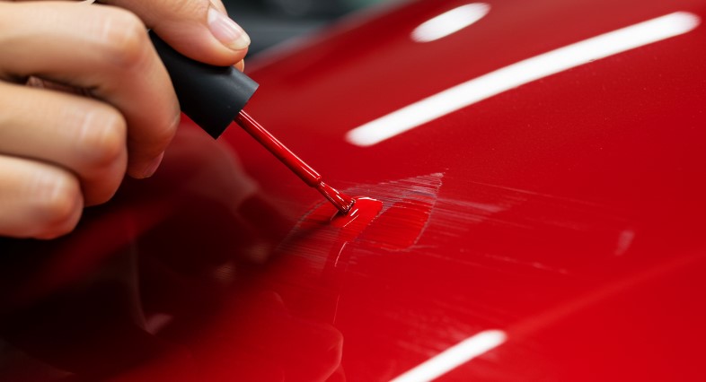 A hand meticulously applies touch-up paint to a red car panel