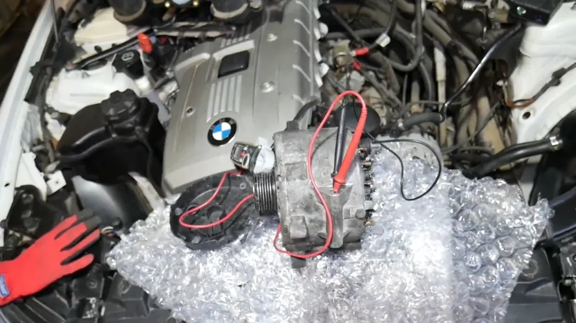 Removed alternator placed near the BMW 6 Series N52 engine, showing part of the electrical fault diagnosis process