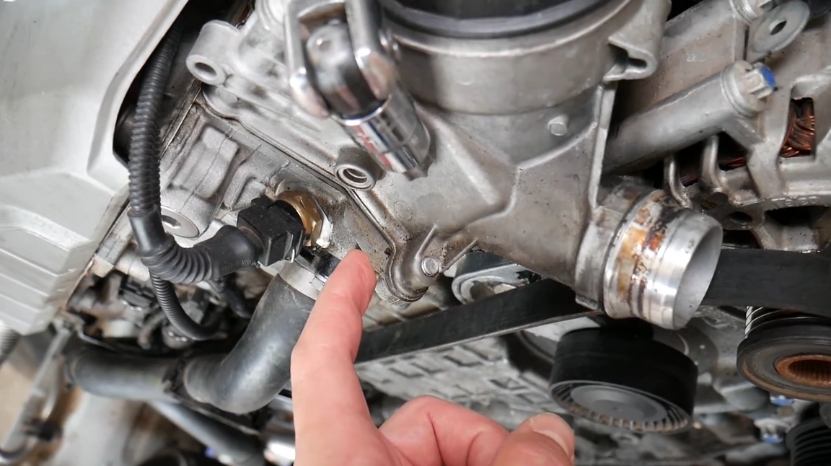 Mechanic points to a common oil leak area on the E63 BMW 6 Series engine near the gasket and belt components