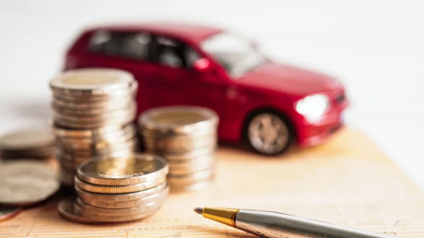 Stacks of coins and a pen in front of a red toy car, symbolizing how buyers manage auto payments
