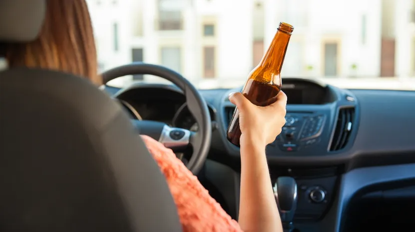 A woman holds a beer bottle while sitting in the driver’s seat, showing the real risks tied to legal drinking and driving
