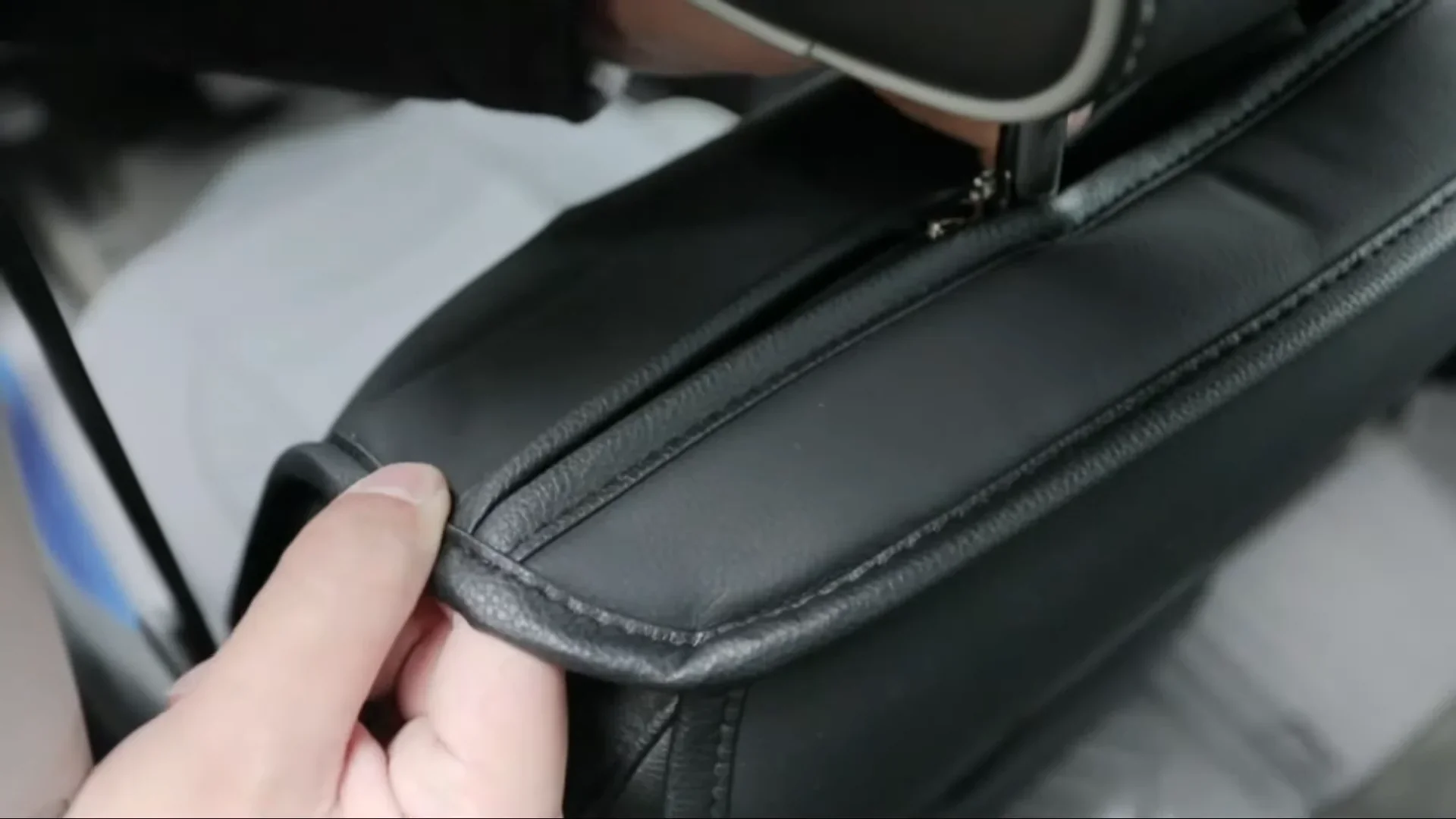 Close up of a hand adjusting a custom-fit black leather seat cover to match the car's original upholstery
