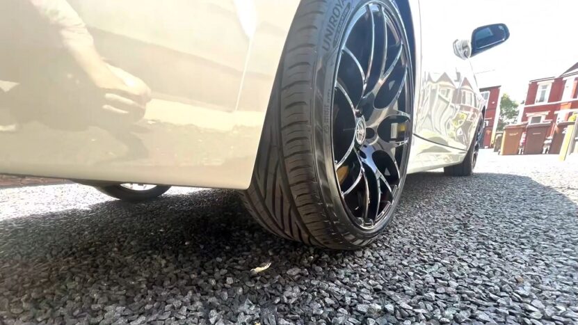 A clean black alloy wheel, parked on gravel