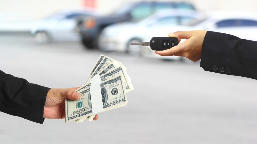 Hand giving cash and another hand offering car keys, showing a car payment exchange