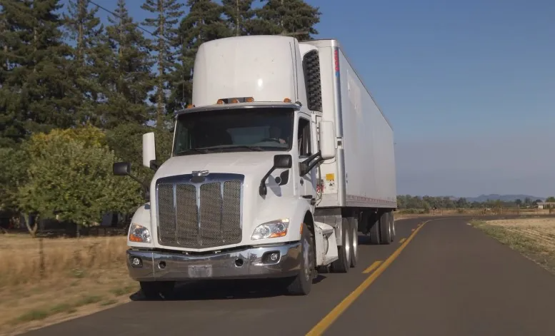 A white refrigerated semi-truck travels down a rural road