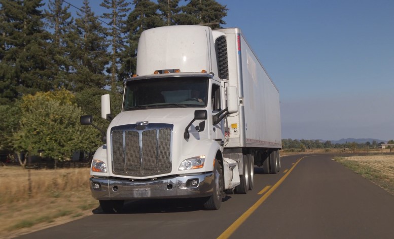 A white refrigerated semi-truck travels down a rural road