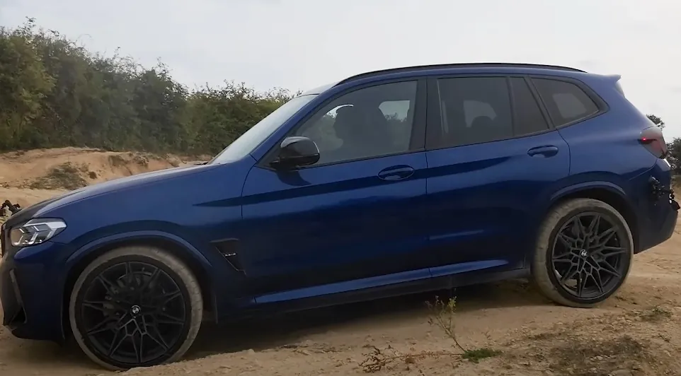 A deep blue BMW X6, navigating a sandy trail