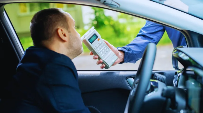 A police officer holds a breathalyzer device up to a male driver during a roadside BAC check