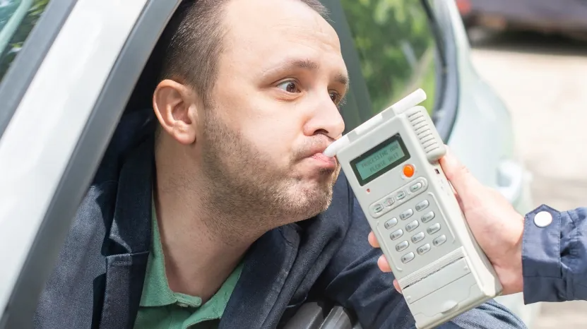 A man blows into a breathalyzer device during a roadside test, illustrating enforcement of the 0.08% legal drinking limit