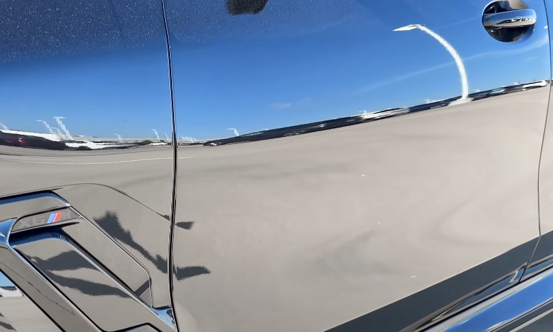 A sleek, dark car, perfectly reflecting the azure sky and distant landscape