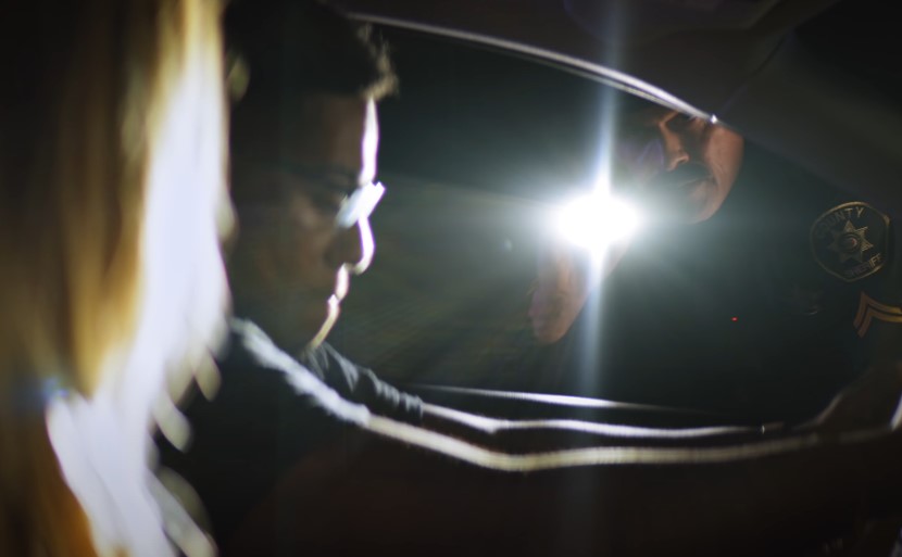 A police officer shines a light into a car at night, illuminating the interior