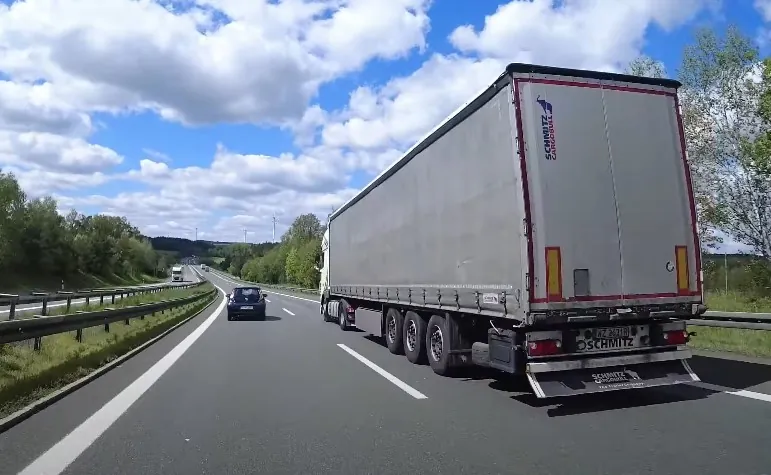 A large, light gray semi-truck travels down a highway
