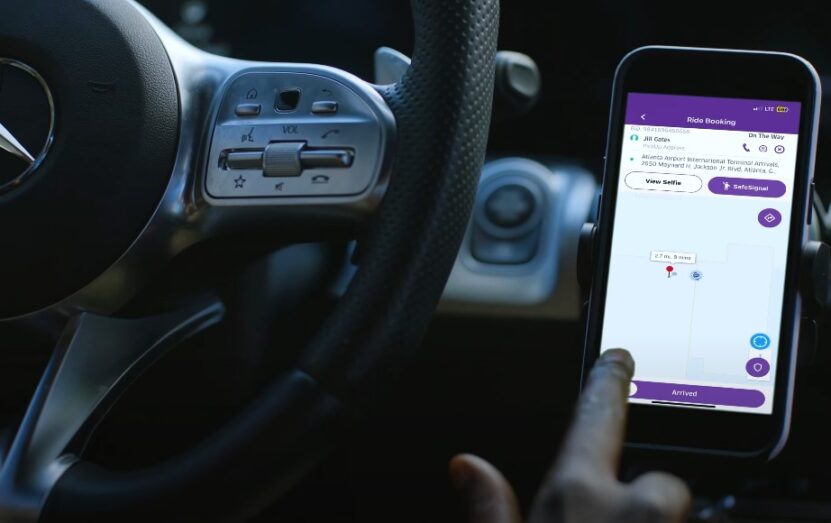 A ride-booking app is displayed on a smartphone, positioned in a car's dashboard mount
