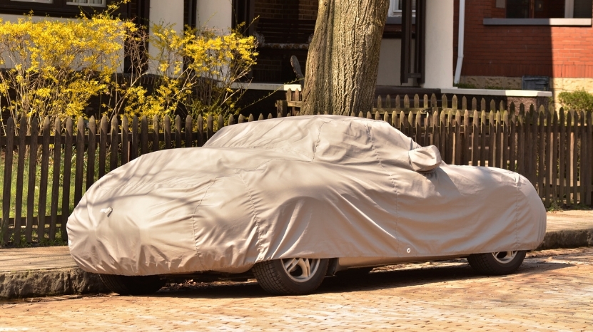 A car parked on a street fully covered with a beige protective cover