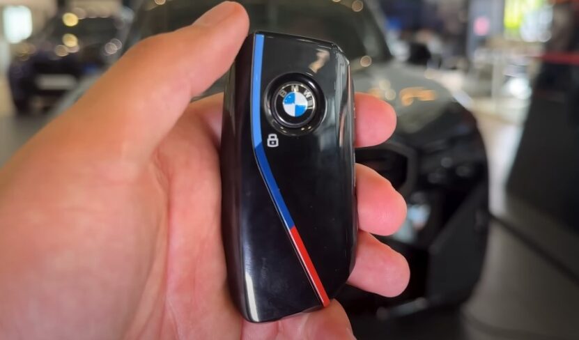 A person holds a BMW key fob in front of a parked BMW car