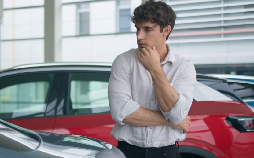 A man contemplates his next car purchase, surrounded by a selection of vehicles