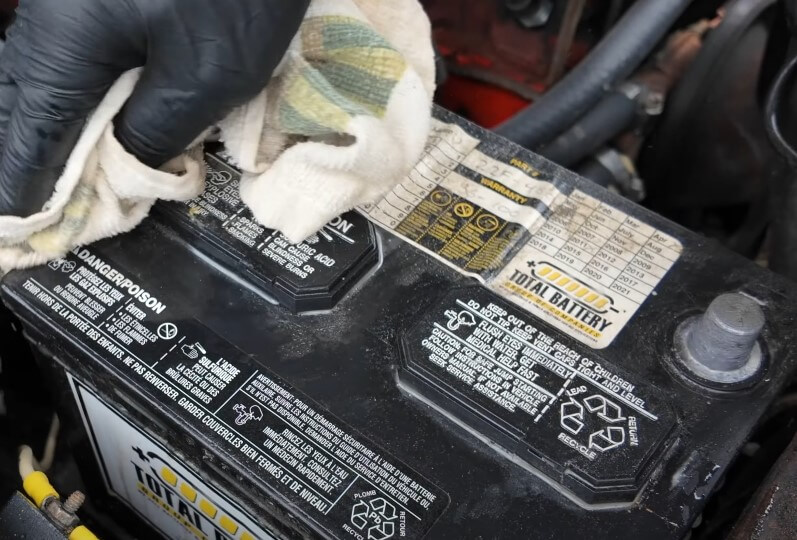 A person using a cloth to clean the battery terminals of a car in a garage setting