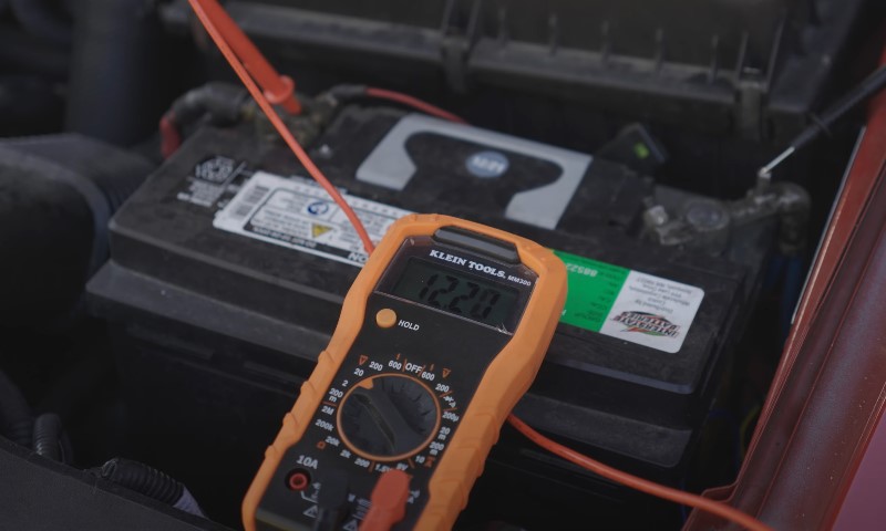 Testing car battery health with a multimeter displaying 12.20 volts