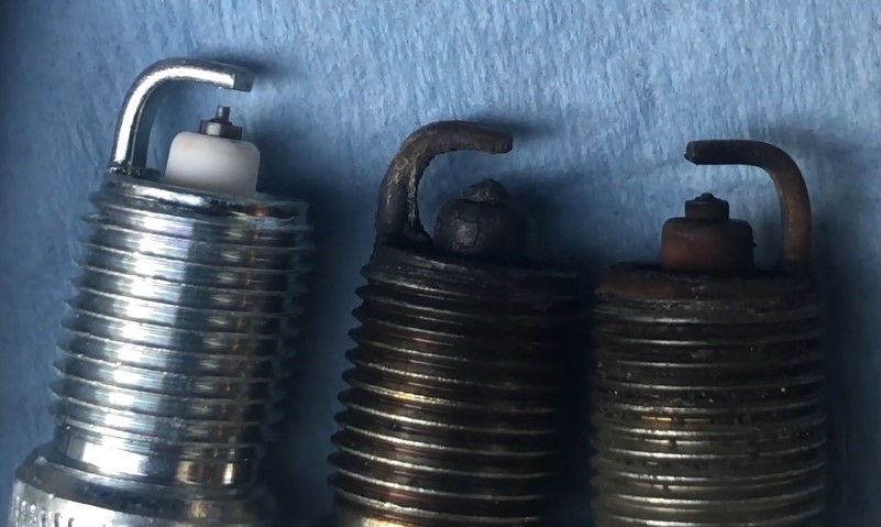Three spark plugs, two old and one brand-new, close up view