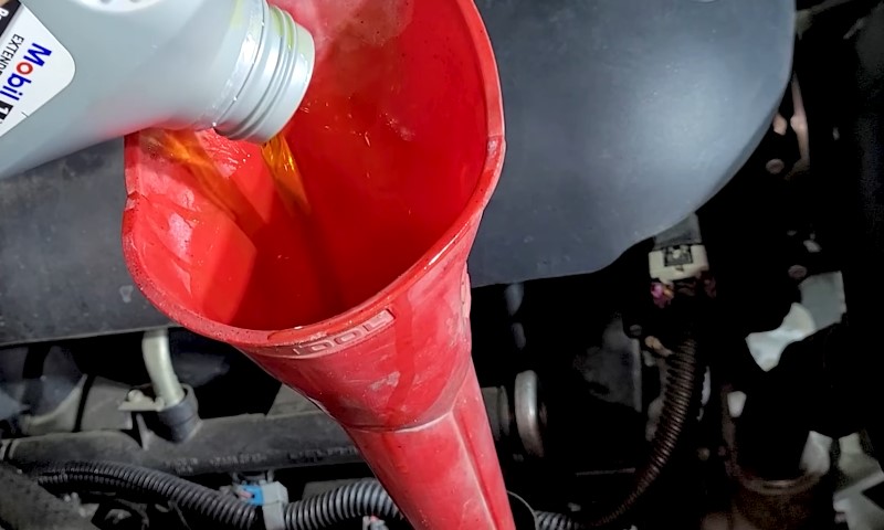 A red funnel is positioned upright as it is being filled with oil from a container above