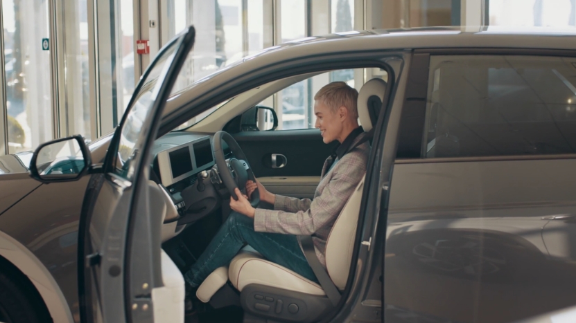 A customer sits in a car inside a dealership while checking the interior