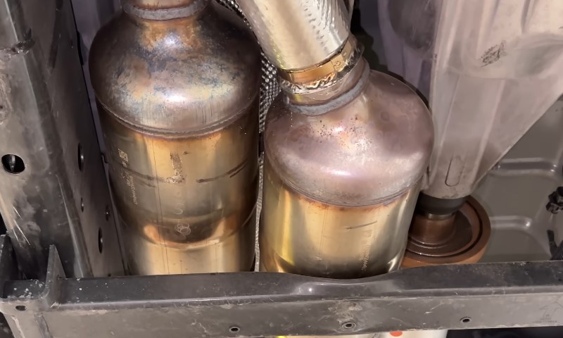 Close-up of two metallic catalytic converters beneath a vehicle