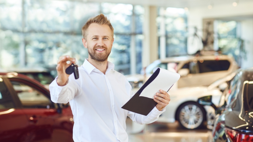 Man in a car showroom holding keys and paperwork