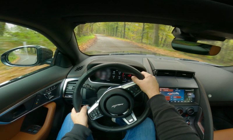 POV view from inside a car driving on a scenic, tree-lined road. Hands grip the wheel